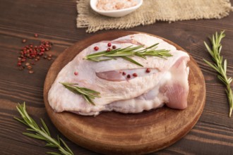Raw Turkey Thigh with spices and rosemary on cutting board on brown wooden background and linen