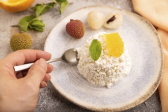 White ?ottage cheese, Curd, with orange and lychee with hand on brown concrete background and