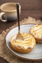French lemon tart with meringue on brown wooden background, cup of coffee, linen textile, side