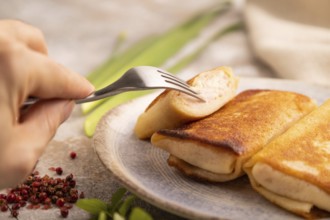 Fried crispy pancakes with meat and cheese with hand on brown concrete background and linen textile