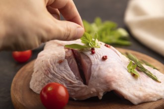 Raw Turkey Thigh with spices and rosemary on cutting board on black concrete background with hand