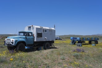 An old lorry with a camper van on a flowering meadow under a blue sky, beekeeper, near Karakert,