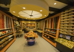 A shop with a variety of cheeses arranged on shelves and tables, illuminated in warm light, Delft,