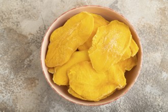 Dried Mango in ceramic bowl on brown concrete background. Top view, close up, flat lay. healthy