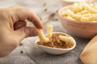 Corn flakes sticks with hand with caramel in ceramic bowl on gray concrete background and orange