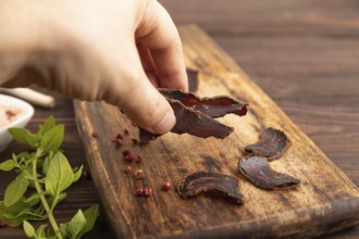 Armenian Basturma dried meat with hand on wooden cutting board with pepper and herbs on brown