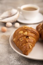 Croissant on white plate on brown concrete background and linen textile, cup of coffee, side view,