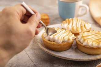 French lemon tart with meringue with hand on brown concrete background, cup of coffee, orange linen