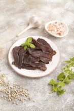 Armenian Basturma dried meat on plate with pepper and herbs on brown concrete background. Side