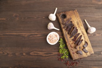Armenian Basturma dried meat on wooden cutting board with pepper and herbs on brown wooden
