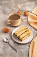 Waffles with caramel on brown concrete background and orange linen textile, cup of coffee, side
