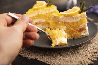 Lemon cake with hand on black concrete background and linen textile, cup of coffee, side view,