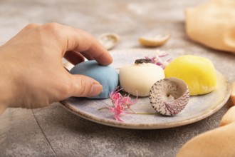 Japanese Mochi Cakes with hand on brown concrete background and orange textile, side view, close