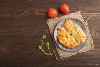 Baked chicken meat with cheese and tomatoes on brown wooden background and linen textile. top view,