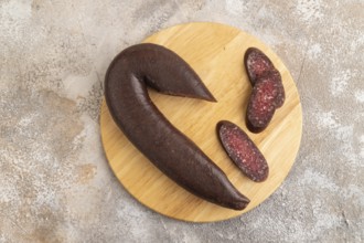 Sujuk sausage on wooden cutting board with pepper and herbs on brown concrete background. Top view,