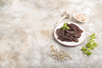 Armenian Basturma dried meat on plate with pepper and herbs on brown concrete background. Side