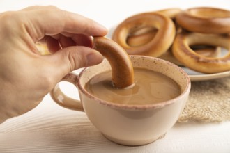 Homemade Ring Bagel with hand with cup of coffee on white wooden background and linen textile. side