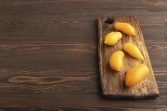 Yellow tomatoes on cutting board on brown wooden background. Side view, copy space. healthy food,
