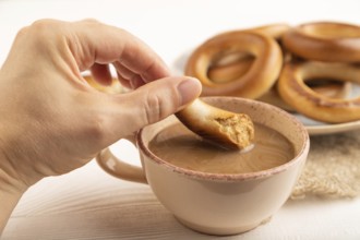 Homemade Ring Bagel with hand with cup of coffee on white wooden background and linen textile. side