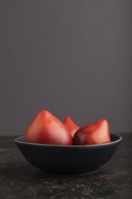 Red Heart shape tomatoes in blue bowl on black concrete background. Side view, copy space. healthy
