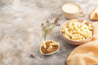 Corn flakes sticks with caramel in ceramic bowl on gray concrete background and orange linen