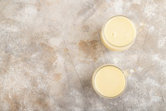 Organic non dairy banana and soy milk in glass on brown concrete background. Vegan healthy food