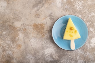 Yellow Cake pop with sprinkles on blue ceramic plate on brown concrete background, top view, flat