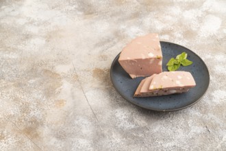 Mortadella sausage on wooden cutting board with pepper and herbs on brown concrete background. Side