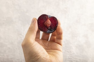 Purple Plum Cut in half with hand on gray concrete background. Side view, close up. healthy food,