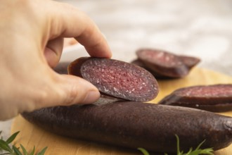 Sujuk sausage with hand on wooden cutting board with pepper and herbs on brown concrete background.