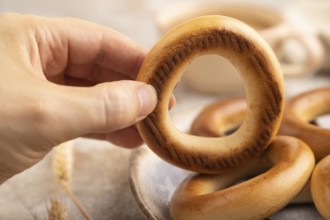 Homemade Ring Bagel with hand with cup of coffee on brown concrete background and linen textile.