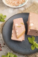 Mortadella sausage on plate with pepper and herbs on brown concrete background and linen textile.