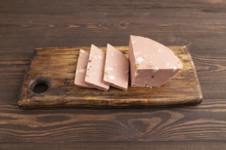 Mortadella sausage on wooden cutting board with pepper and herbs on brown wooden background. Side