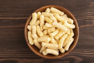Corn flakes sticks with caramel in wooden bowl on brown wooden background. Top view, flat lay, copy