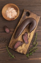 Sujuk sausage on wooden cutting board with pepper and herbs on brown wooden background. Top view,
