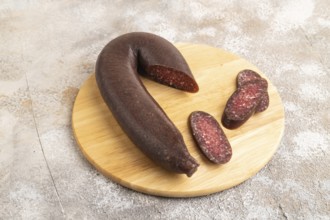 Sujuk sausage on wooden cutting board with pepper and herbs on brown concrete background. Side