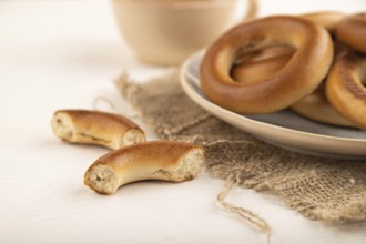 Homemade Ring Bagel with cup of coffee on white wooden background and linen textile. side view,
