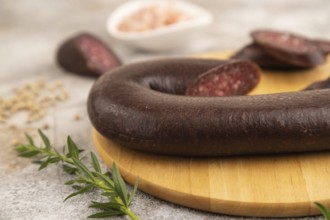 Sujuk sausage on wooden cutting board with pepper and herbs on brown concrete background. Side