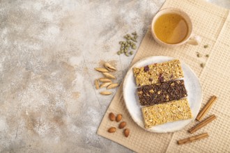 Granola bars with caramel, nuts, flakes in ceramic plate on brown concrete background, beige linen