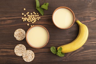Organic non dairy banana and soy milk in clay cup on brown wooden background. Vegan healthy food
