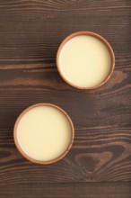 Organic non dairy banana and soy milk in clay cup on brown wooden background. Vegan healthy food