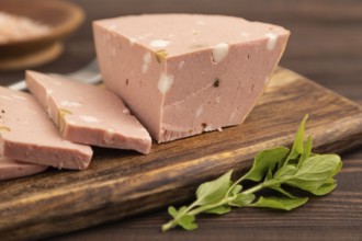 Mortadella sausage on wooden cutting board with pepper and herbs on brown wooden background. Side