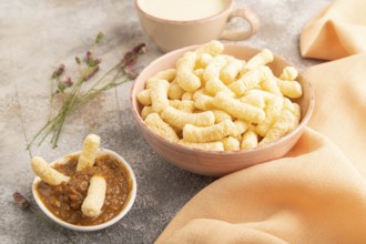 Corn flakes sticks with caramel in ceramic bowl on gray concrete background and orange linen