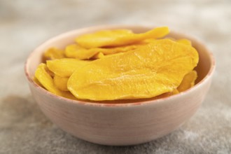 Dried Mango in ceramic bowl on brown concrete background. Side view, close up, selective focus.