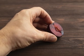 Purple Plum Cut in half with hand on brown wooden background. Side view, close up. healthy food,