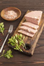 Mortadella sausage on wooden cutting board with pepper and herbs on brown wooden background. Side