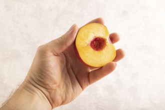 Peach Cut in half with hand on brown concrete background. Side view, copy space. healthy food,
