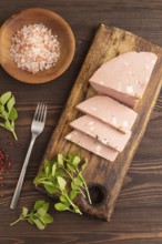 Mortadella sausage on wooden cutting board with pepper and herbs on brown wooden background. Top