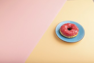 Pink Donut with sprinkles on blue ceramic plate on blue and orange pastel paper background, side