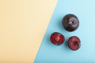 Purple Plum Cut in half on orange and blue pastel paper background. Top view, flat lay, copy space.